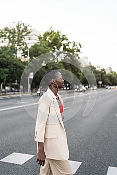 Side view of an elegant young african american adult woman looking forward crossing the street in the city