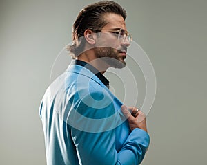 side view of elegant young man with glasses looking to side and fixing suit