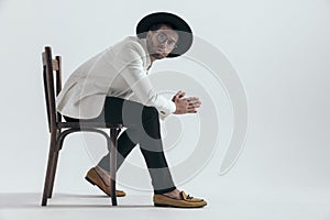 side view of elegant young man with hat and glasses sitting