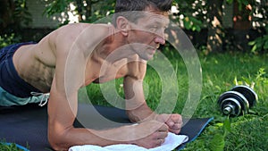 Side view endurant fit sportsman in plank position exercising outdoors looking away. Strong confident Caucasian adult