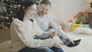 Side view of excited happy pregnant woman looking at positive pregnancy test sitting with smiling man at Christmas tree
