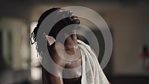 Side view exhausted handsome African American sportsman wiping sweat with towel exhaling. Portrait of motivated endurant