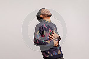Side view extremely excited happy african guy with dreadlocks laughing holding his belly with hands, funny joke, anecdote photo