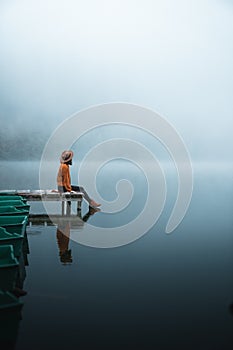 Side view of fashioned young woman sitting on wooden dock looking at view on a misty morning photo