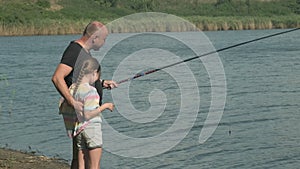 Side view of father with kid girl fishing together standing on river bank