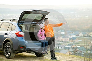 Side view of father with little daughter standing near car with open trunk and enjoying nature. Concept of weekend with family