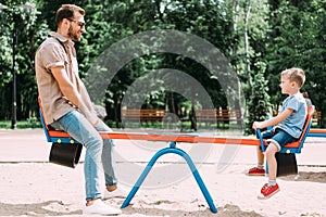 side view of father and son having fun on swing at playground