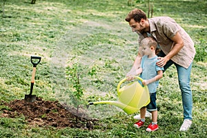 side view of father and son watering seedling with watering can