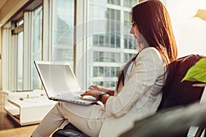 Side view of female boss wearing stylish elegant white suit holding laptop on her lap working in modern office