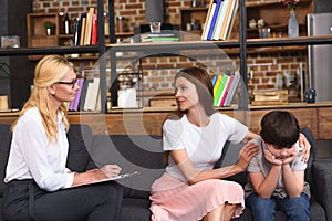 side view of female counselor talking to mother while she embracing stressed son on therapy