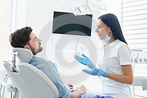 Side view of female dentist advicing and gesturing to client sitting in dental chair