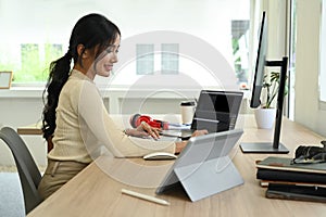Side view of female freelancer editing video and audio footage with computer software at modern office