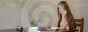 Side view of female freelancer working on her project with laptop and office supplies