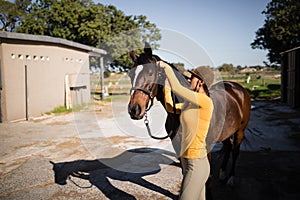 Side view of female jockey fastening bridle on horse