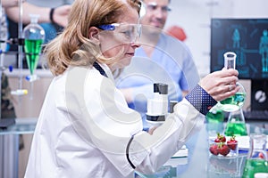 Side view of female scientist holding a test tube with green solution