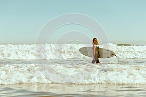 Side view of female surfer in wetsuit with his surfboard entering the sea. Surfing on waves