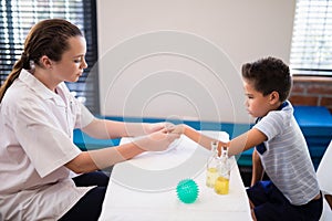 Side view of female therapist examining hand while boy sitting at table