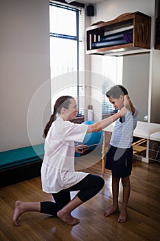 Side view of female therapist kneeling while examining boy