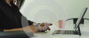 Side view of female using smartphone while working with laptop on worktable