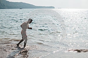 Side view of a fit asian man running by the beach, slightly silhouetted against the sun