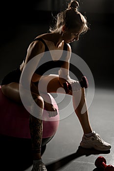 Side view of fit beautiful young woman exercising with dumbbells on fitness ball