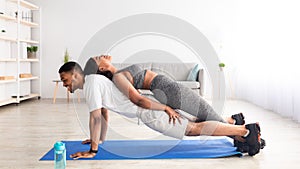 Side view of fit black couple doing partner yoga, standing in plank on mat at home, panorama