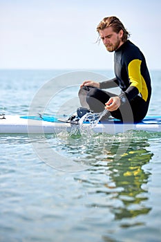 side view on fit man splashing with water while sitting on surfboard, having rest