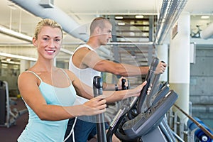 Side view of a fit young couple working on x-trainers at the gym