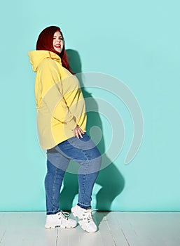 Side view of a flirtatious curvy young woman putting one foot on toe in front of other. Full length shot isolated on blue