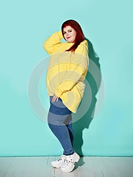 Side view of a flirtatious curvy young woman putting one foot on toe in front of other. Full length shot isolated on blue