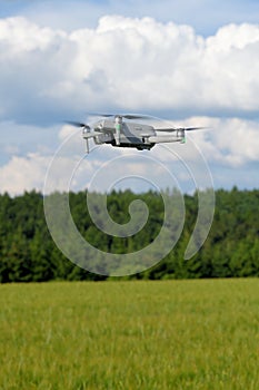 Side view of a flying modern UAV drone on yellow corn field a blue sky background