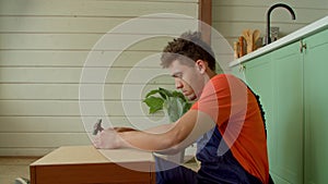 Side view of focused black man nailing bedside table rear panel with hammer