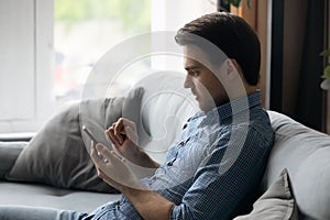 Side view focused man using smartphone, sitting on couch