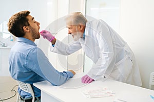 Side view of focused mature adult male doctor taking swab sample of mouth with cotton stick for DNA tests, COVID-19.