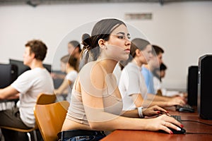 Side view on focused teenager female student sitting at desk in computer class, preparing for exam