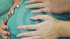 Side view of four female caucasian hands caressing belly of the expectant woman. Young women having pre-bith party and