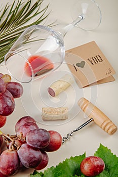 side view of fresh grape , small postcard, bottle screw with wine corks and a wine glass lying on white background