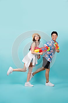 Side view of full length portrait of Young Asian couple walking and holding water gun isolated on blue background
