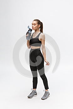 Side view full length portrait of a young healthy sports woman holding a water bottle isolated on a white background