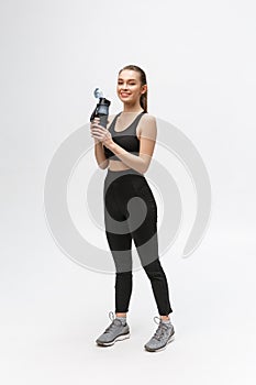 Side view full length portrait of a young healthy sports woman holding a water bottle isolated on a white background