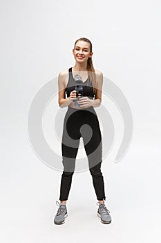 Side view full length portrait of a young healthy sports woman holding a water bottle isolated on a white background