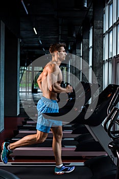 Side view full length of young man in sportswear running on treadmill at gym