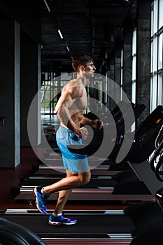 Side view full length of young man in sportswear running on treadmill at gym