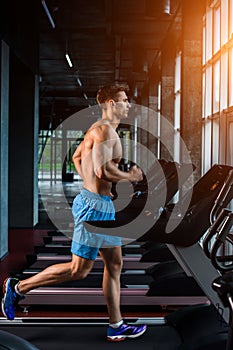 Side view full length of young man in sportswear running on treadmill at gym