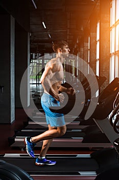 Side view full length of young man in sportswear running on treadmill at gym