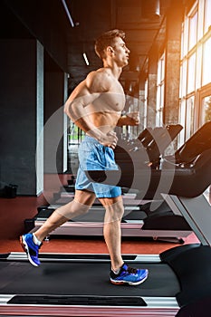 Side view full length of young man in sportswear running on treadmill at gym