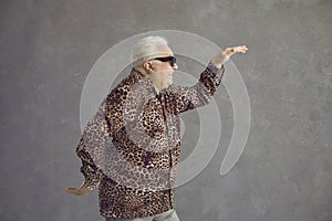 Side view of funny senior man in leopard shirt dancing in studio with gray background