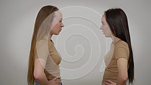 Side view furious angry twin sisters yelling shouting gesturing arguing at grey background. Medium shot of dissatisfied