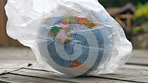 Side view of the globe of Earth in polyethylene disposable package on wooden background. Concept of ecological problems