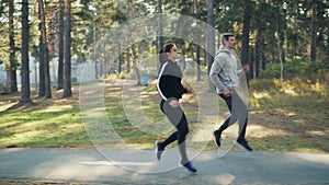 Side view of good-looking young people girl and guy doing sports in park running and jumping together on road on warm